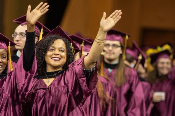 Students in caps and gowns waving at graduation